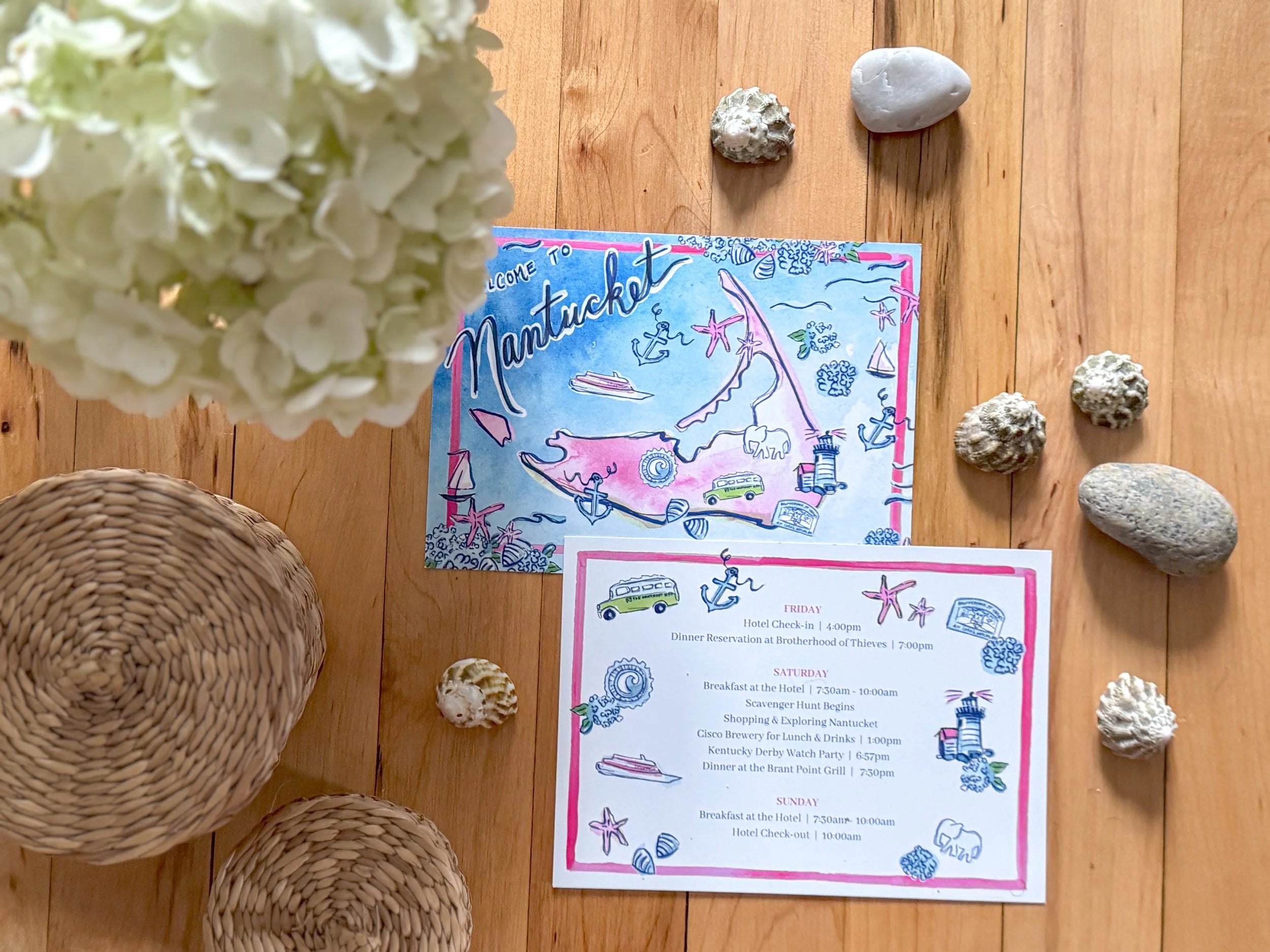 Nantucket-themed invitations on a wooden surface with flowers and stones.