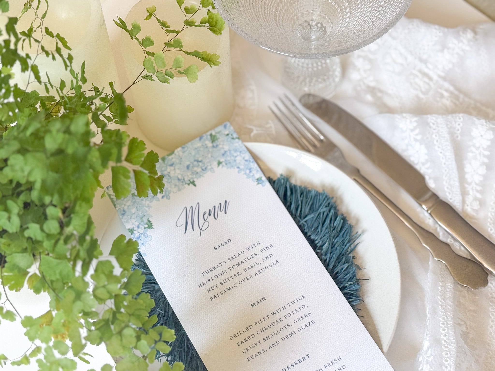 Table setting with a menu card, plate, and cutlery on a white tablecloth.