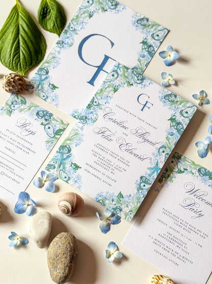 Wedding invitations with blue monogram GF and watercolor floral border, arranged with paper and leaves